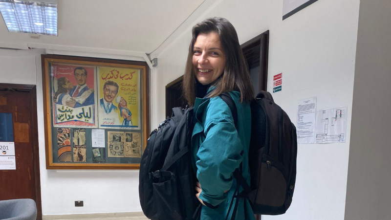 Justyna Mackiewicz standing inside a building carrying two backpacks at smiling.